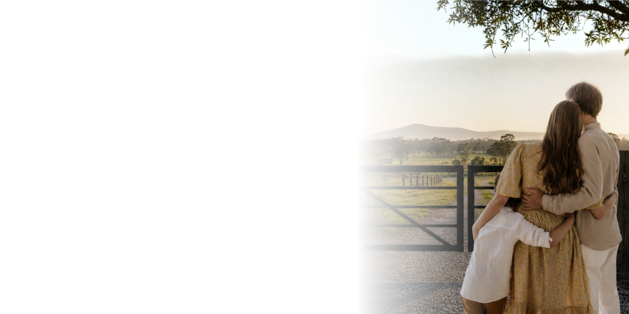 Two people embracing in a field with a sunset and wooden gate in the background